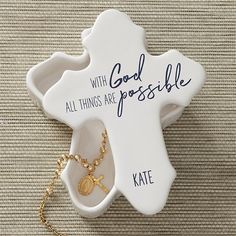 a white ceramic cross with gold accents and a chain on the bottom that says, with god all things are possible