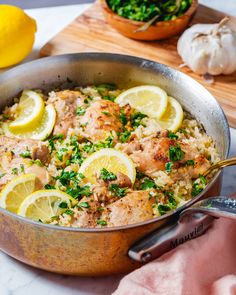 a pan filled with chicken and rice covered in lemons, parsley and herbs