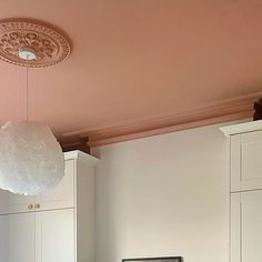 a kitchen with white cupboards and pink painted ceiling above the stovetop, is pictured in this image