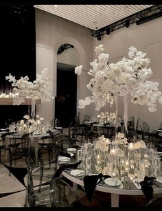 a room filled with tables and chairs covered in white flower centerpieces, surrounded by tall glass vases