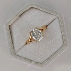 an engagement ring with a cushion cut diamond on it in a white velvet presentation box