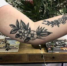 a woman's arm with flowers and leaves on it, in front of a table