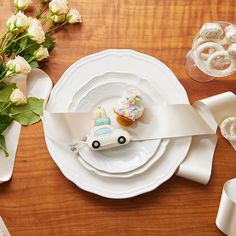 a table set with white plates, napkins and cupcakes in the shape of a car