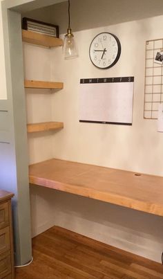 a clock mounted to the side of a wall next to a wooden desk and shelf