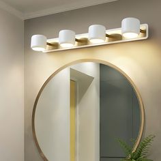 a bathroom with a round mirror and lights on the wall next to a potted plant