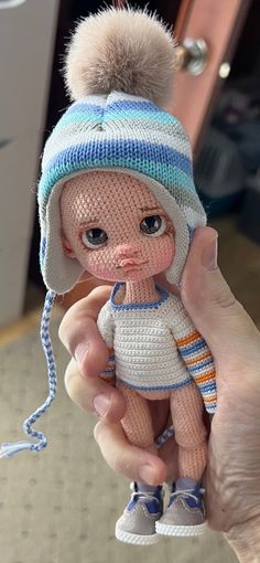 a hand holding a small doll with a hat and scarf on it's head