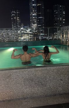 two people in a swimming pool at night with skyscrapers in the backgroud