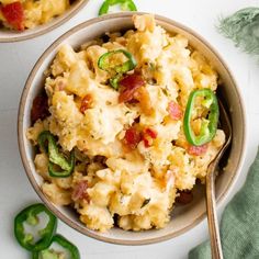 two bowls filled with macaroni and cheese on top of a white table next to green peppers