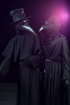 two people dressed in black standing next to each other with masks on their faces and hands