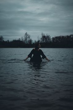 a person sitting in the water with their back turned to the camera, wearing a black shirt