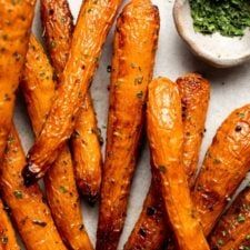 some carrots are on a white surface with herbs and seasoning next to them