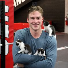 a young man holding two kittens in his arms while standing next to a pole