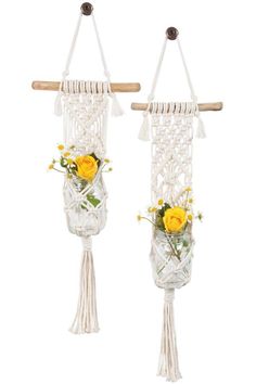 two white macrame hangings with yellow flowers and greenery in them on a wooden stick