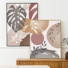 two framed art prints on a wall above a wooden dresser with vases and plants