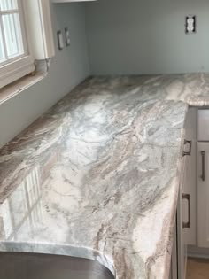 a marble counter top in a kitchen with white cupboards and drawers on either side