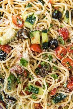 a pasta dish with zucchini, olives, tomatoes and parmesan cheese