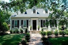 a white house with black shutters on the front and side windows is surrounded by trees