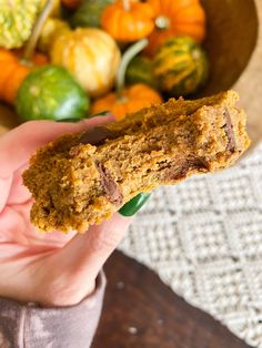 a hand holding a cookie in front of a bowl of pumpkins