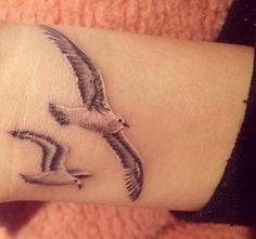 a small tattoo on the wrist of a woman with a bird flying above her arm