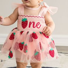 a baby girl wearing a pink dress with strawberries on it