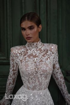 a woman wearing a white dress with long sleeves and sheer lace on the top, standing in front of a green door