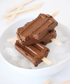 two pieces of chocolate ice cream sitting on top of an ice cube with wooden sticks