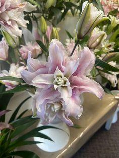 pink and white flowers are in a vase on a table with greenery behind them