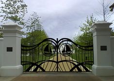 an iron gate is open to reveal a driveway with trees in the backgroud