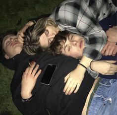 three people laying on the ground with their arms around each other and one person holding an iphone