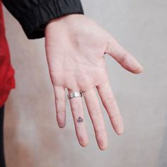 a person's hand with a small triangle tattoo on their left thumb and finger