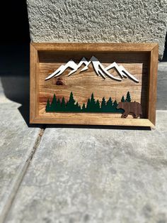 a wooden frame with mountains, trees and a bear in the woods on it's side