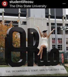 a woman in a white dress is sitting on top of a large black sign that reads, the ohio state university