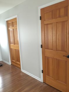 an empty room with two wooden doors and hard wood flooring on the other side