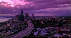 an aerial view of a city at dusk with clouds in the sky and cars on the road