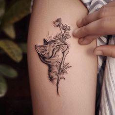 a woman's arm with a small tattoo of a cat and flowers on it