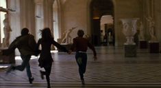 three people are running in the middle of a room with statues on either side of them