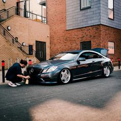 a man kneeling down next to a black car in front of a red brick building