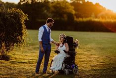 a man in a blue suit standing next to a woman in a wheelchair on top of a grass covered field