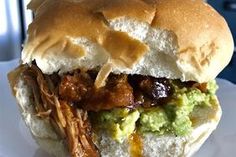 a pulled pork sandwich with guacamole and mustard on a white paper plate