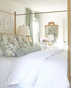 a bed with white linens and pillows in a bedroom next to a mirror on the wall