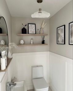 a white toilet sitting in a bathroom next to a shelf filled with vases and pictures