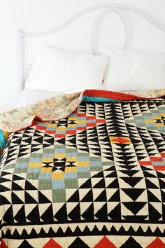 a bed with a black, white and orange quilt on it's headboard