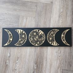 three phases of the moon on a black and gold metal wall art piece with wood grain flooring