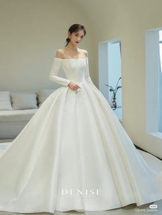 a woman in a white wedding dress standing next to a couch and looking at the camera