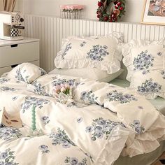 a bed with white sheets and blue flowers on it in a room next to a dresser