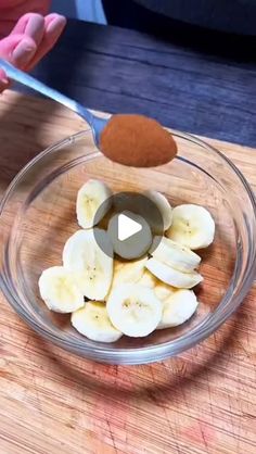 someone is cutting bananas into small pieces in a glass bowl with a spoon on top