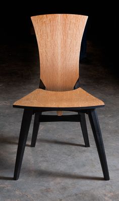 a wooden chair sitting on top of a cement floor next to a black object with a wood seat