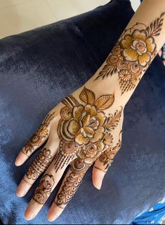 a woman's hand with hennap and flowers on the palm, sitting on a blue cushion