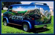 an old blue van painted with mountains and trees on it's side in the grass