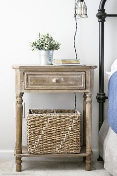 a nightstand with a basket on it next to a bed